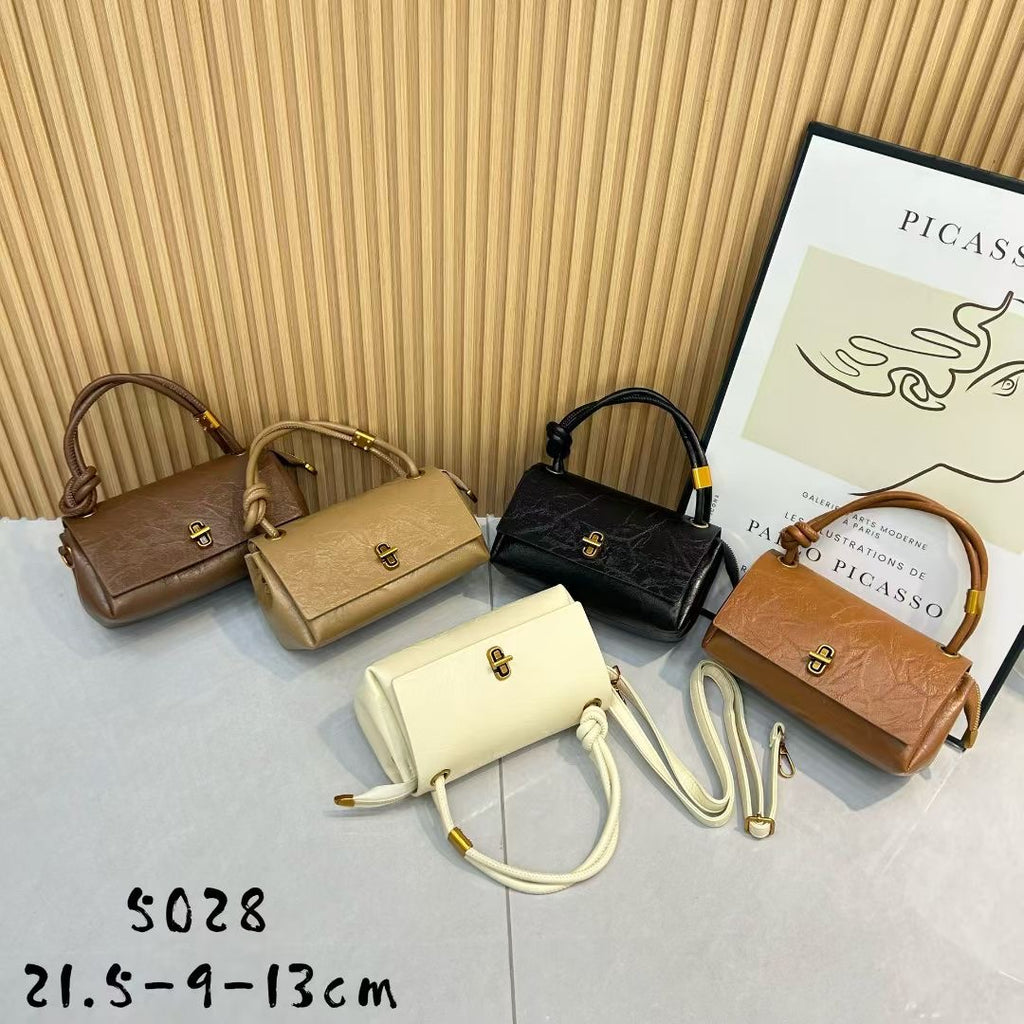 Five handbags in different colors arranged on a surface with a Picasso poster in the background.