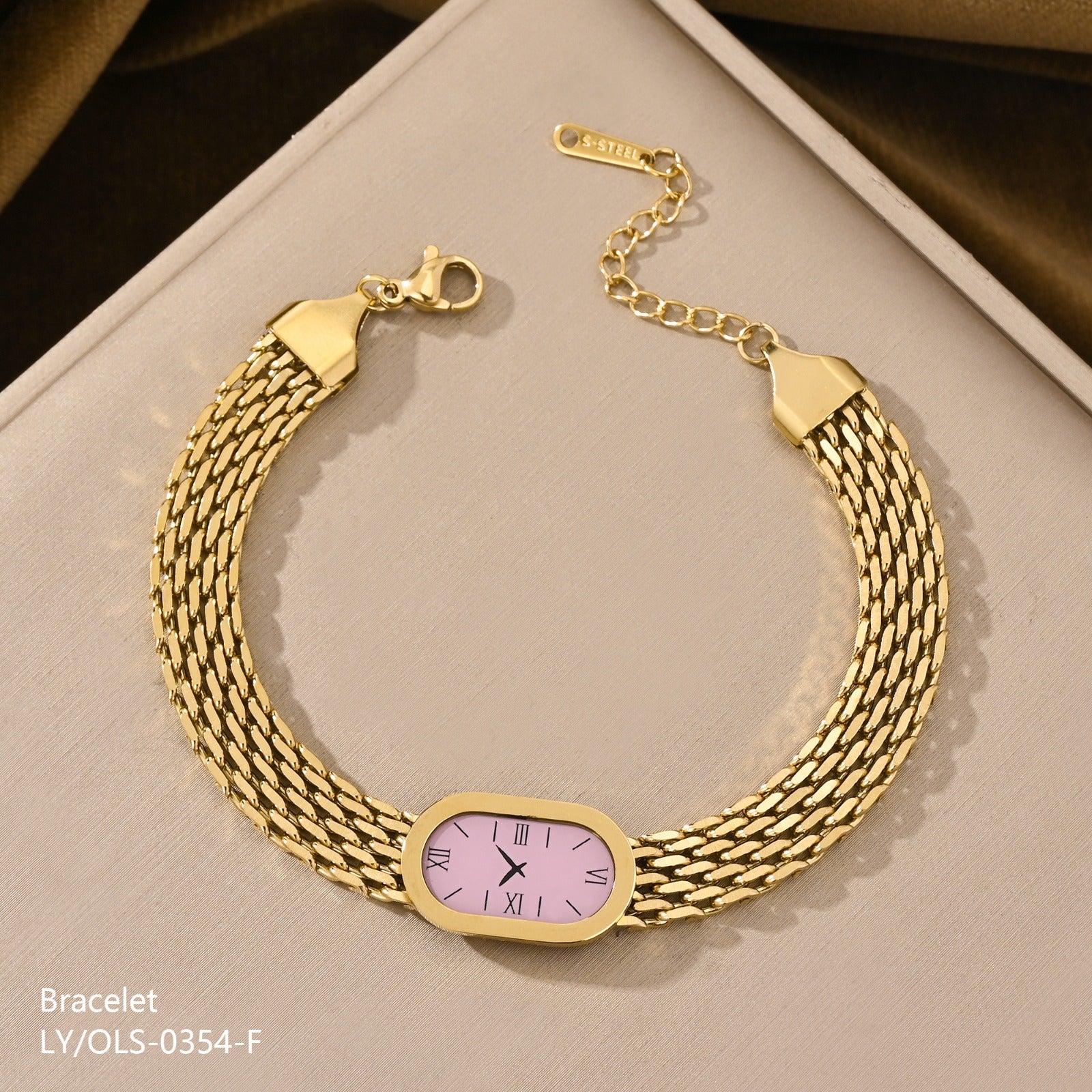 Gold bracelet with a pink face on a beige surface