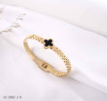 Gold bracelet with a black clover charm on a white background