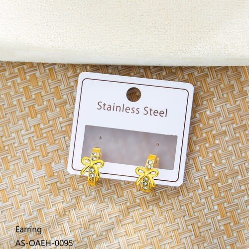 Gold bow-shaped earrings on a white card with 'Stainless Steel' text, placed on a woven surface.